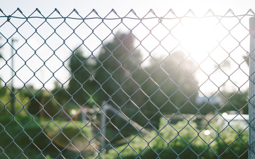 Galvanized chain link fence with grass and sunlight behind it
